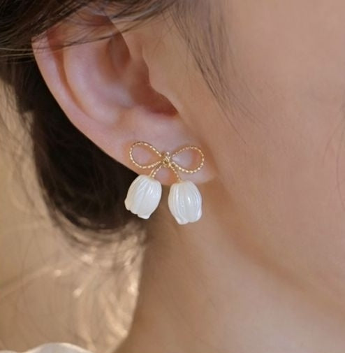 Close-up of gold tone bow knot stud earrings with glossy white pearl petal charms – everyday earrings for Indian women